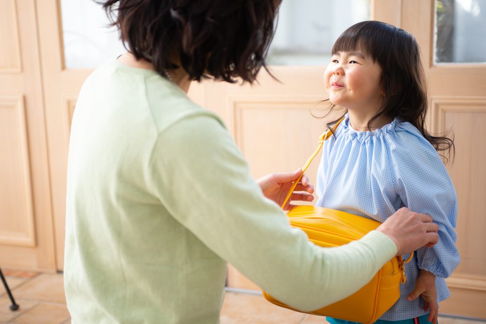お母さんが園児に通園カバンを掛けてあげる様子
