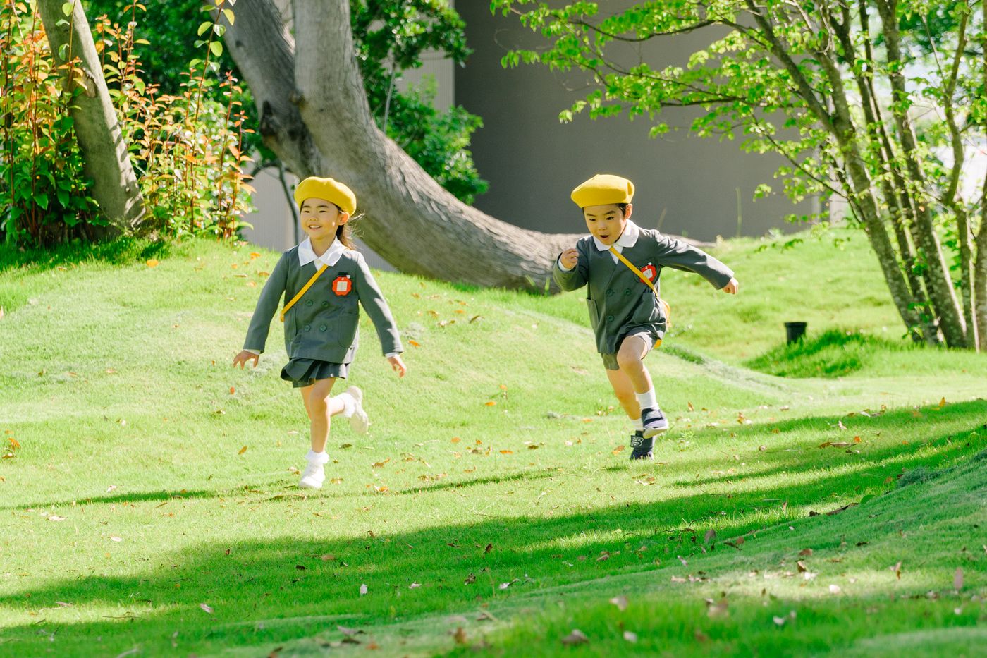 芝生を走る、制服と黄色い帽子の園児2人