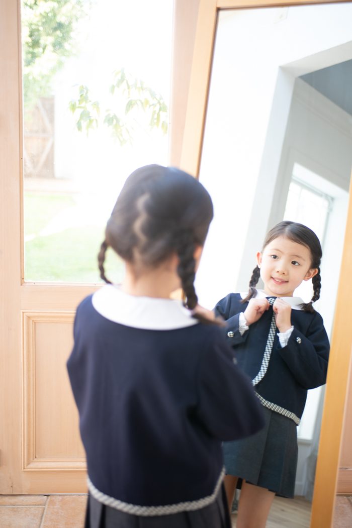 鏡の前で身支度をする園児服の女の子